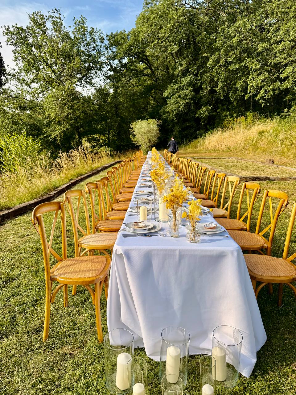Wedding dinner table set with candles along a grass avenue through the woodland at Les Cazettes